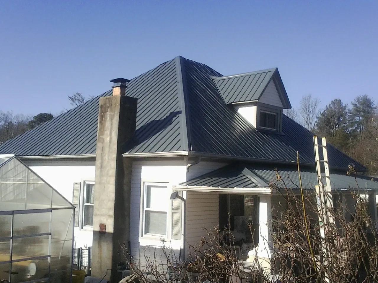 Dark blue standing seam metal roof on a white farmhouse with dormer — Slate & Tile Roof Repair by Roofing Brothers in Spring Arbor