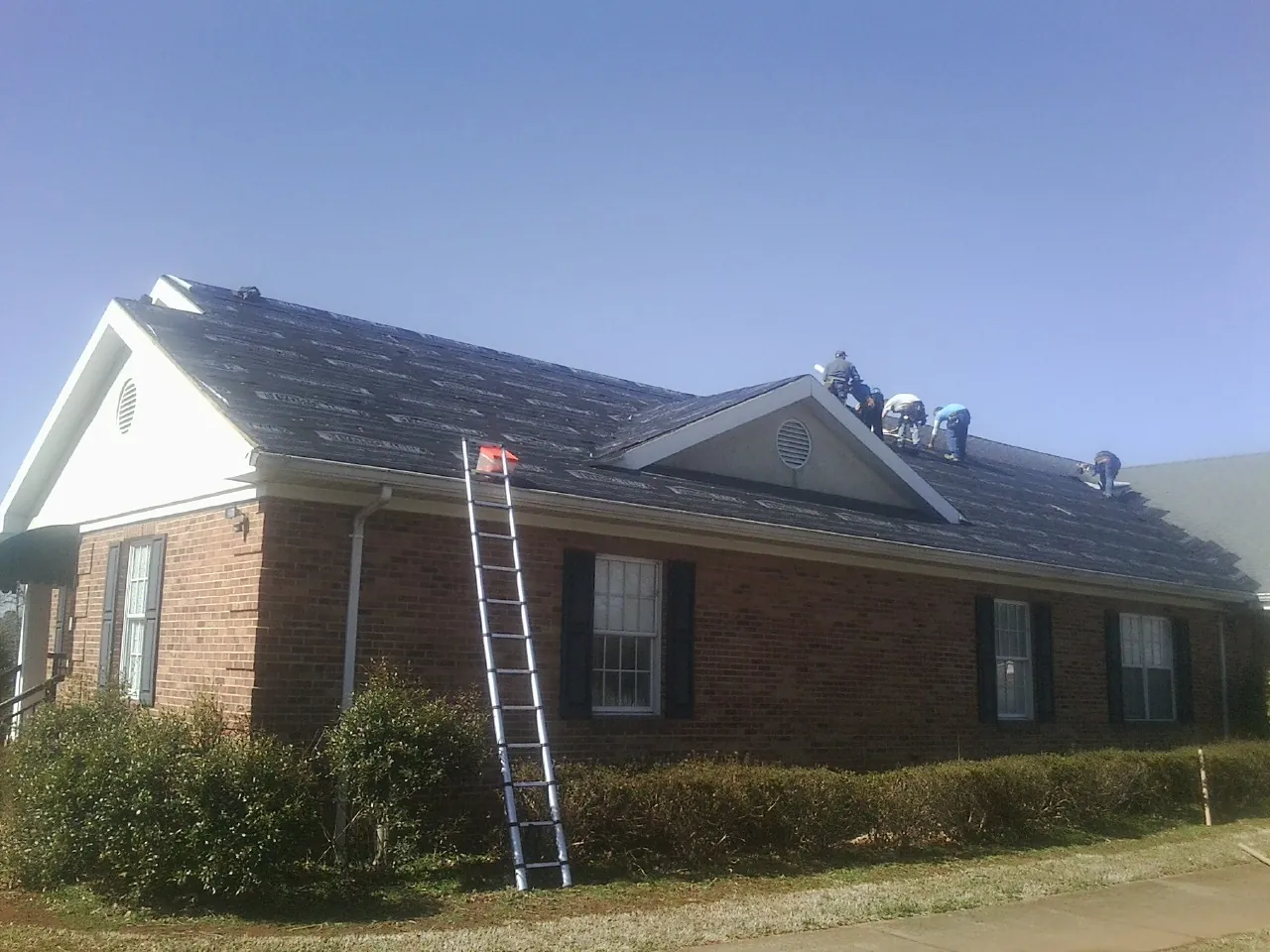 Crew tearing shingles off a brick ranch roof with a ladder set — Metal Roof Repair work by our crew in Spring Arbor