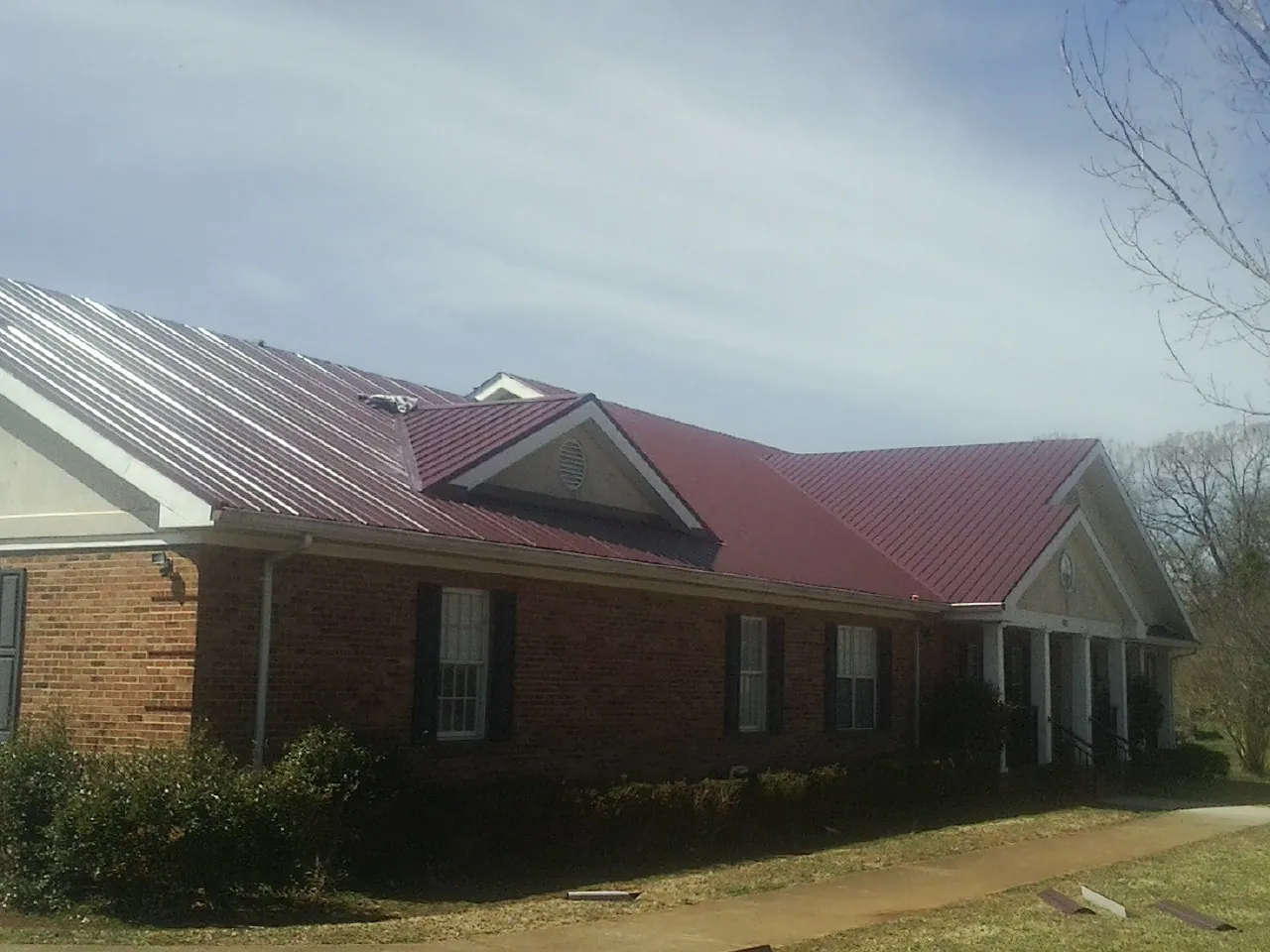 Red metal roof with gabled entries on a long brick building, from a Hail Damage Roof Repair job in Spring Arbor