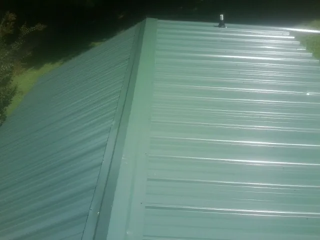 New green metal panels meeting at the ridge of a roof — Flat Roof Repair work by our crew in Spring Arbor