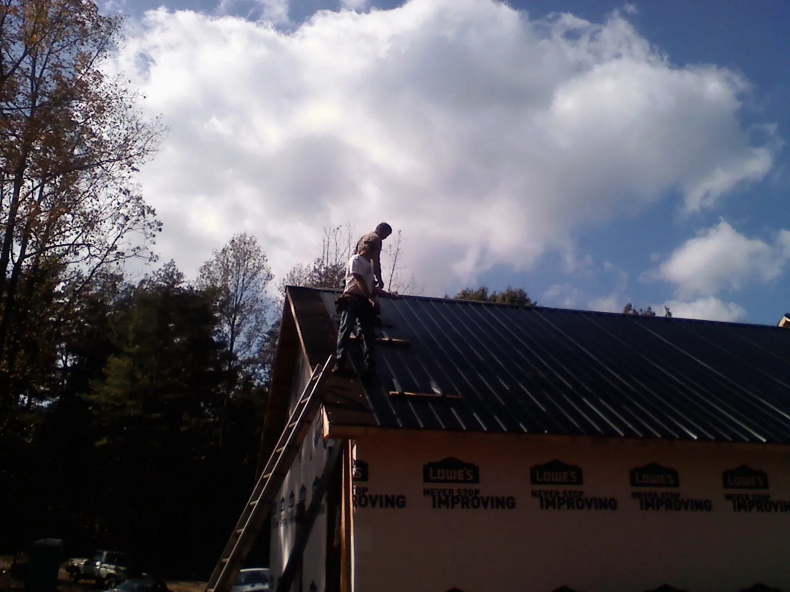 Roofer fastening dark metal panels high against a cloudy sky, from a Roof Inspection job in Spring Arbor