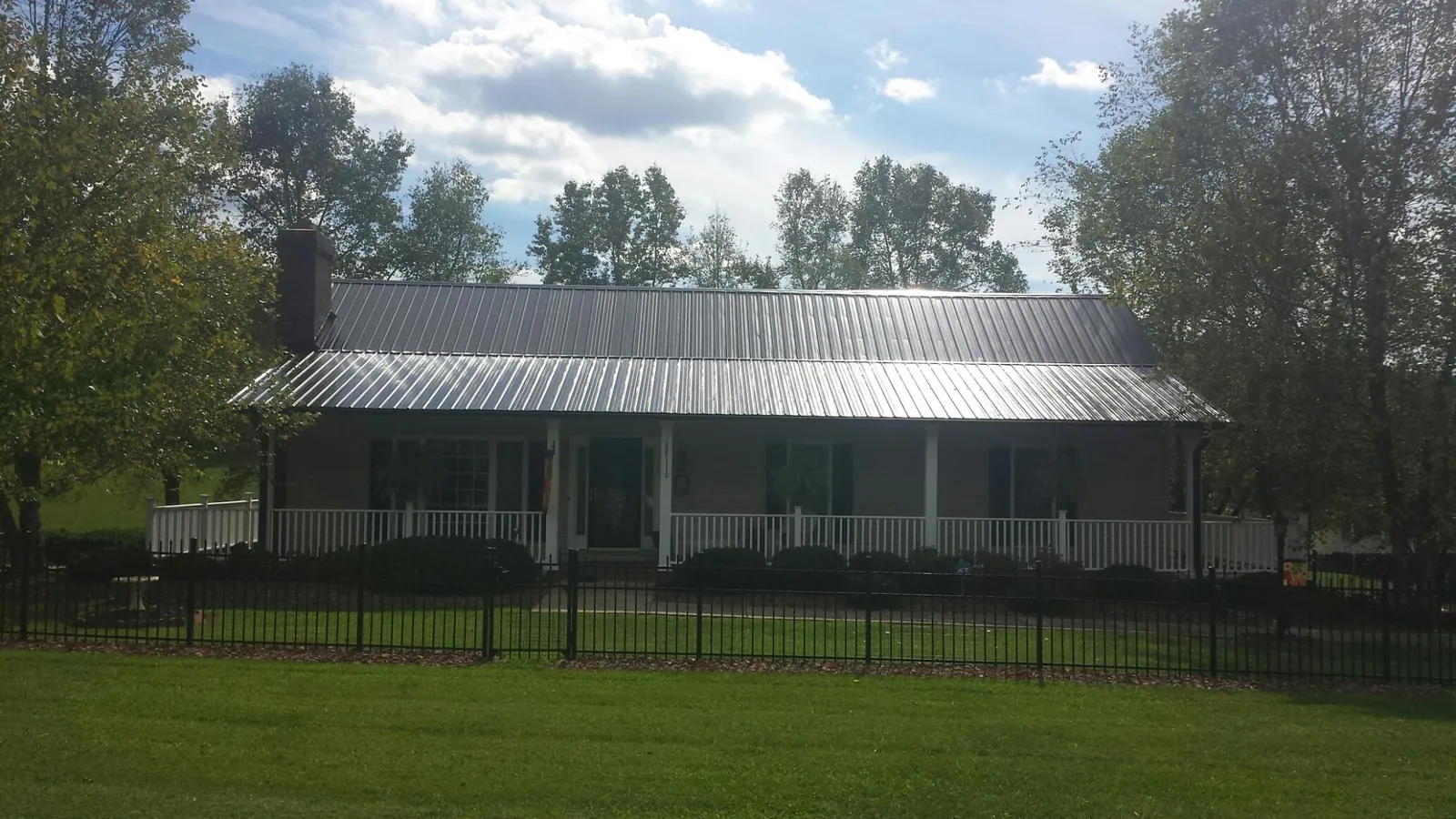 Gray metal roof on a brick ranch with a full width front porch — Gutter Guard Installation work by our crew in Spring Arbor