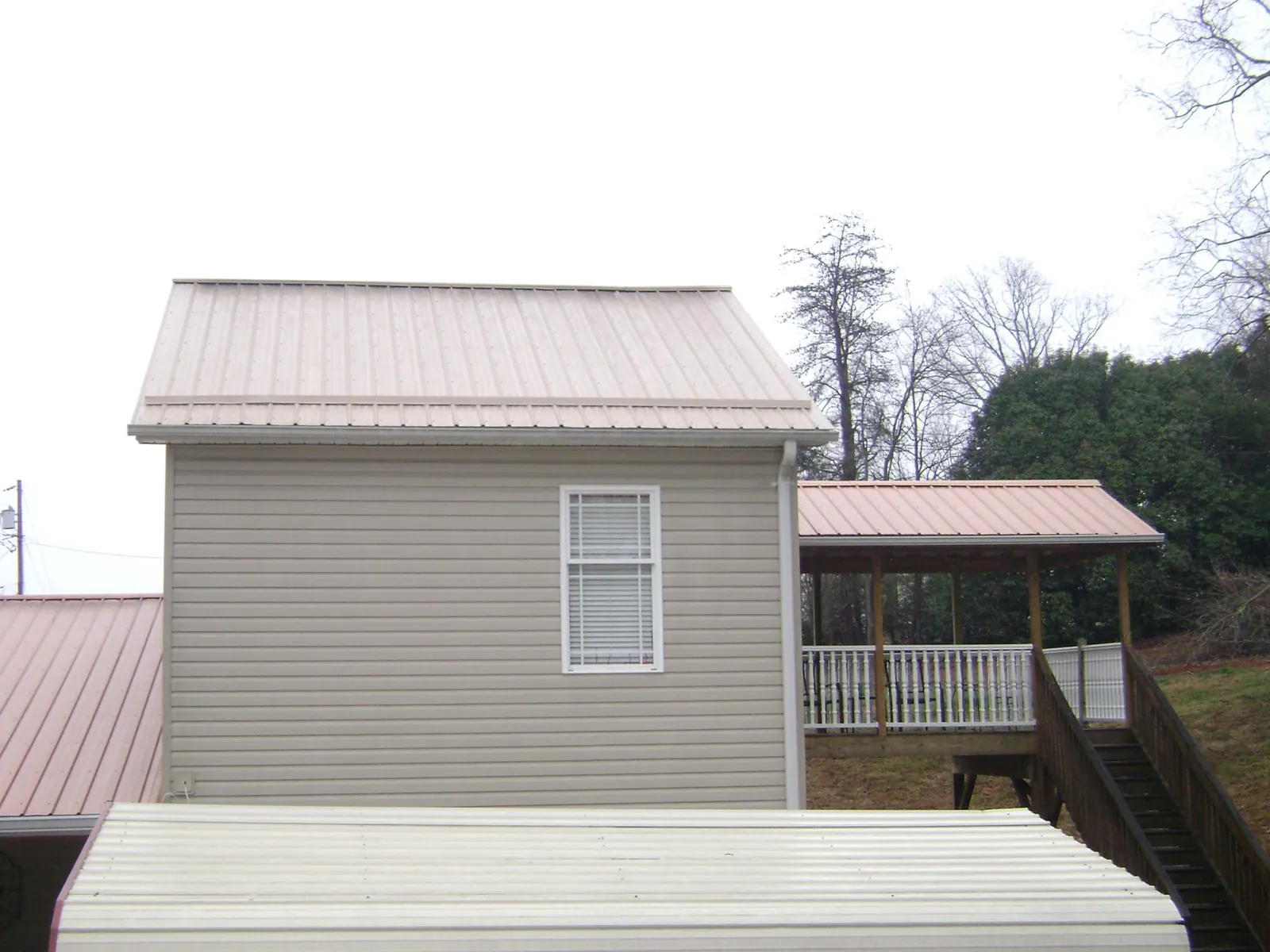 Tan metal roofs on a two story addition and attached porch, from a Roof Replacement job in Spring Arbor